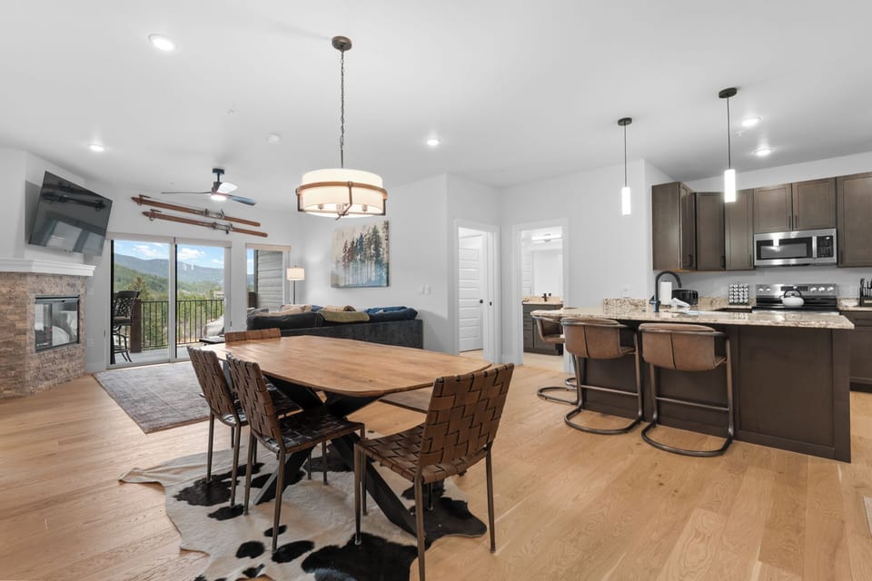 Your open-concept retreat blends mountain-modern elegance with cozy warmth, featuring a spacious dining table, a chef's kitchen, and stunning forest views beyond.