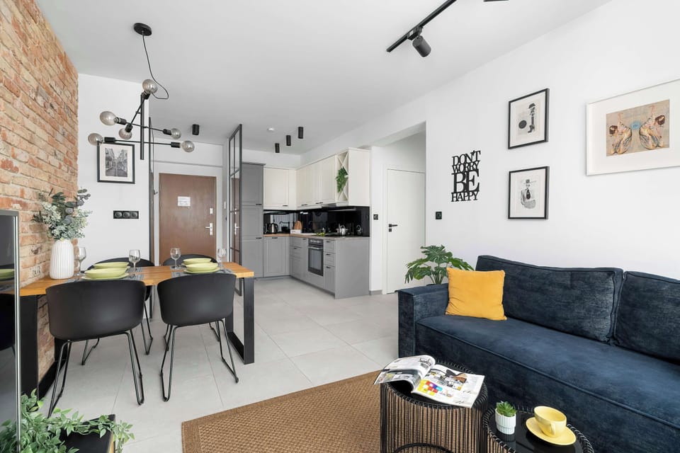 The layout view from the sofa towards the kitchen and dining area emphasizes the spaciousness of the open-plan apartment. Dark furniture contrasts beautifully with the white walls and light-colored flooring.