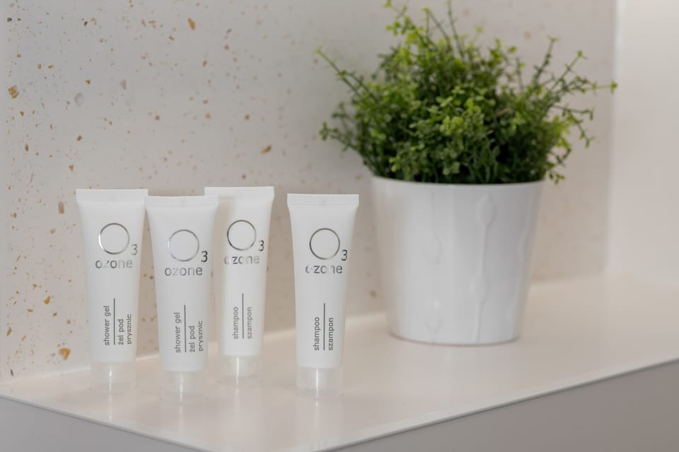 Four small white toiletry tubes are lined up neatly next to a small potted plant on a white shelf. This detail emphasizes the hospitality and attention to guest comfort.