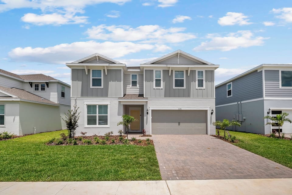 Welcome to this charming two-story home with a light gray exterior and white trim, surrounded by lush landscaping. The inviting entrance and neatly paved driveway promise a delightful stay for all guests.