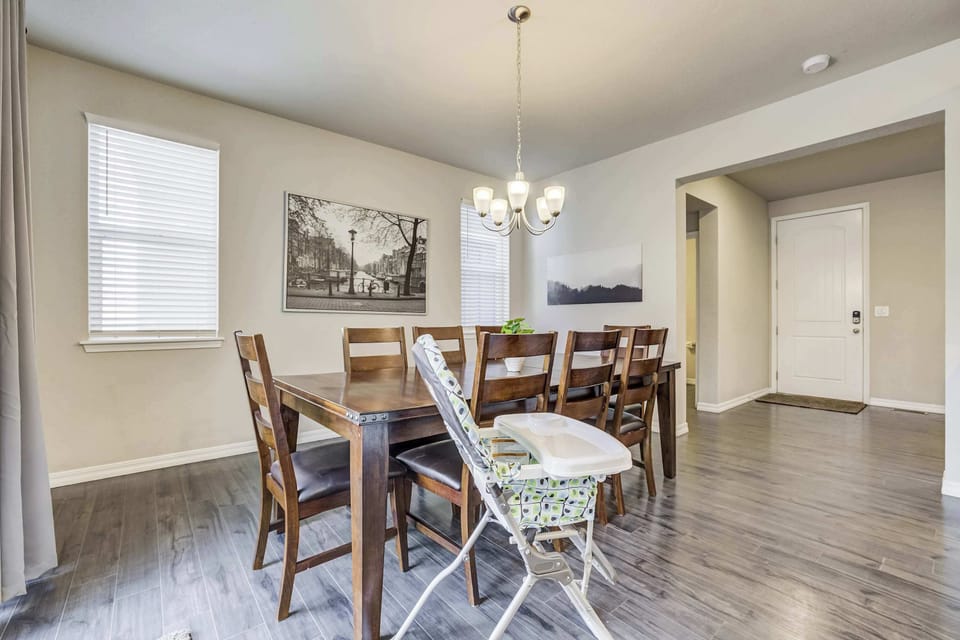 A closer look at the dining setup shows seating for eight around a solid wood table, with a high chair ready for little ones and a framed landscape print adding warmth to the neutral walls. Simple and well-proportioned for the space.

