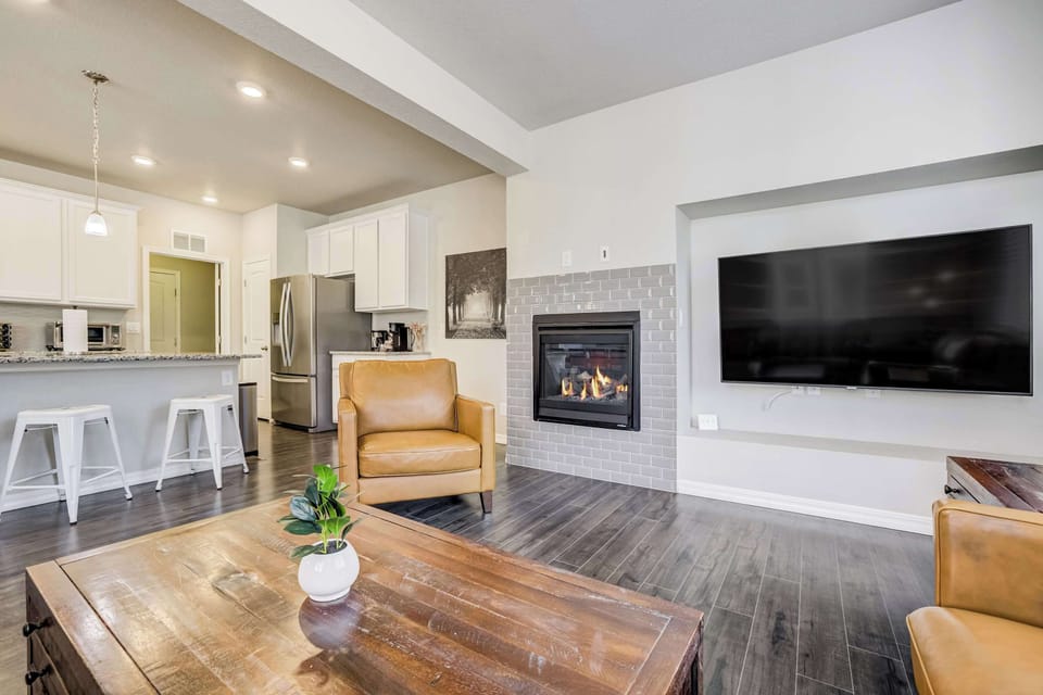 An open-concept layout connects the living area to the kitchen, anchored by a wall-mounted fireplace and TV. White cabinetry, bar seating, and hardwood floors create a bright, functional space with easy flow throughout.
