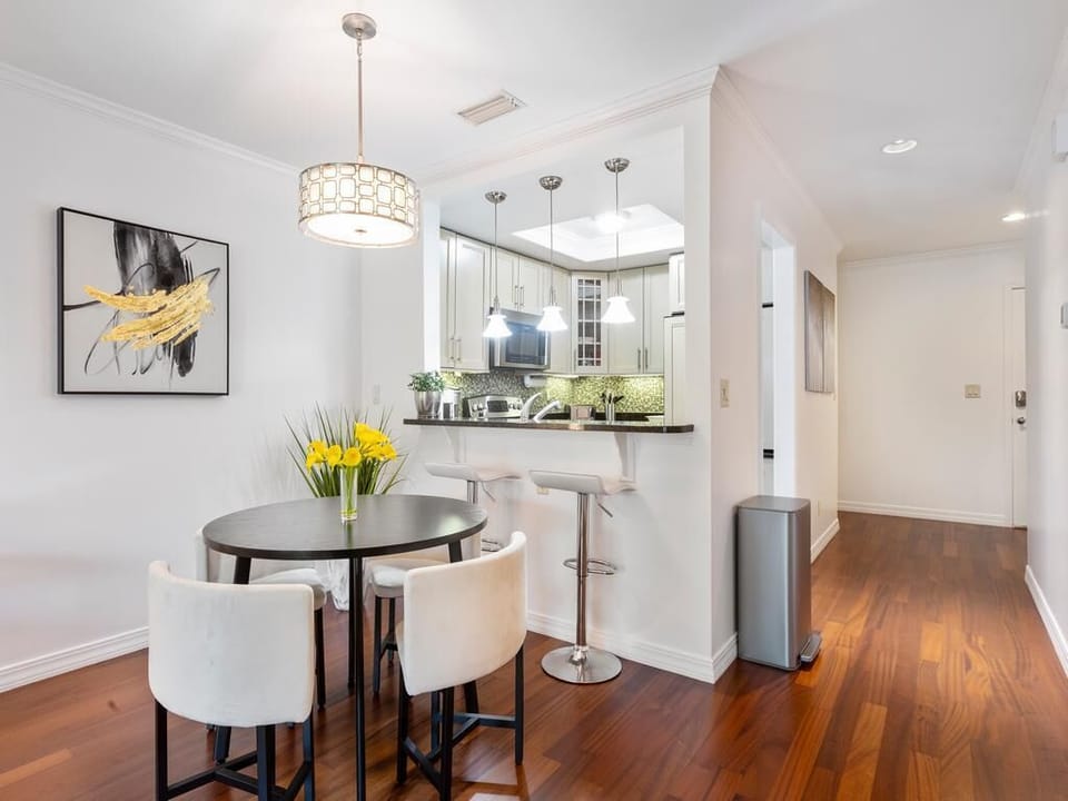Round dark wood dining table with white upholstered chairs beneath a geometric pendant light.