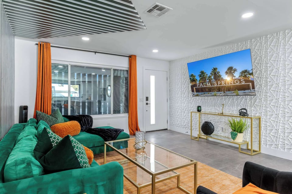 Living room with large-screen wall-mounted TV, textured 3D accent wall, and emerald sectional — settle in and feel the Palm Springs energy