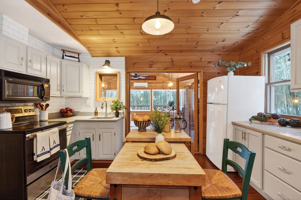 Open kitchen and living space with a central prep island, wood-burning stove, and natural light—easy for cooking, gathering, and everyday cabin living.