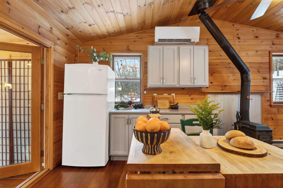 Open kitchen and living space with a central prep island, wood-burning stove, and natural light—easy for cooking, gathering, and everyday cabin living.