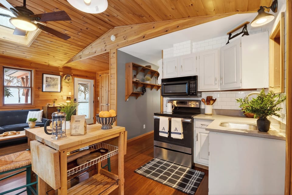 Open kitchen and living space with a central prep island, wood-burning stove, and natural light—easy for cooking, gathering, and everyday cabin living.