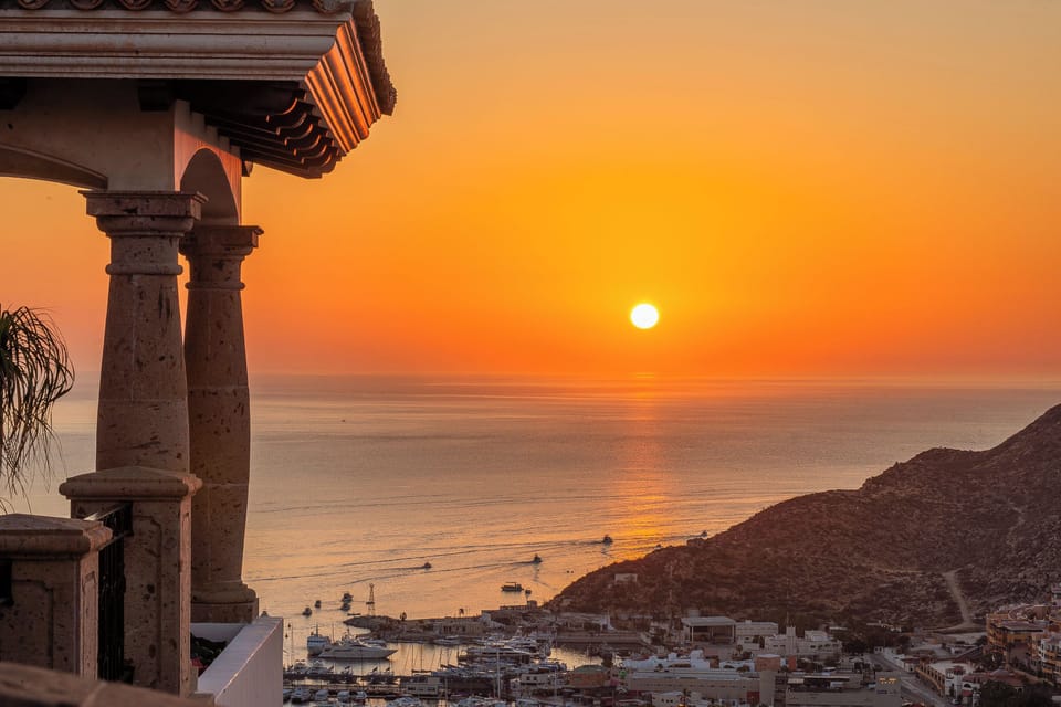 A stunning sunset view over the Mediterranean coastline, with traditional architecture framing the golden horizon and peaceful harbor below.