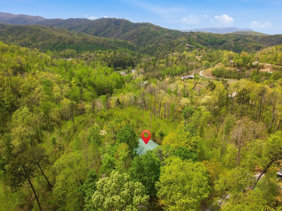 Aerial view showcasing the property's secluded location nestled among rolling mountain ridges and lush spring foliage in a peaceful valley setting.