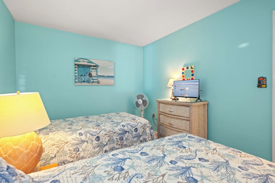 Relax in your coastal-themed twin bedroom with ocean-inspired bedding, flat-screen TV, and cheerful beachy decor that brings seaside vibes indoors.