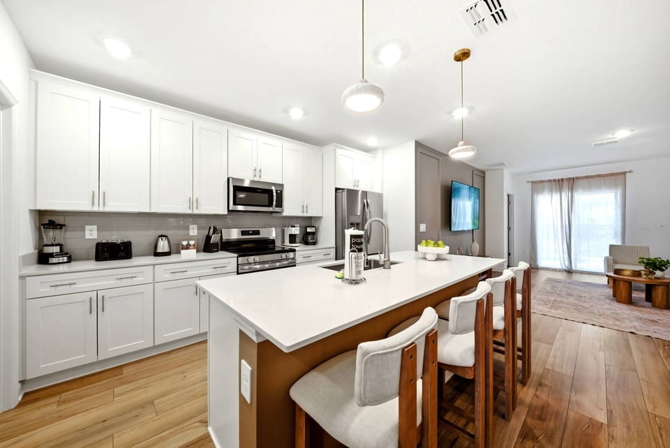 This bright kitchen boasts sleek white cabinetry with warm wood accents for a welcoming feel. The spacious island is perfect for gatherings, and large windows flood the space with natural light, enhancing the inviting decor.