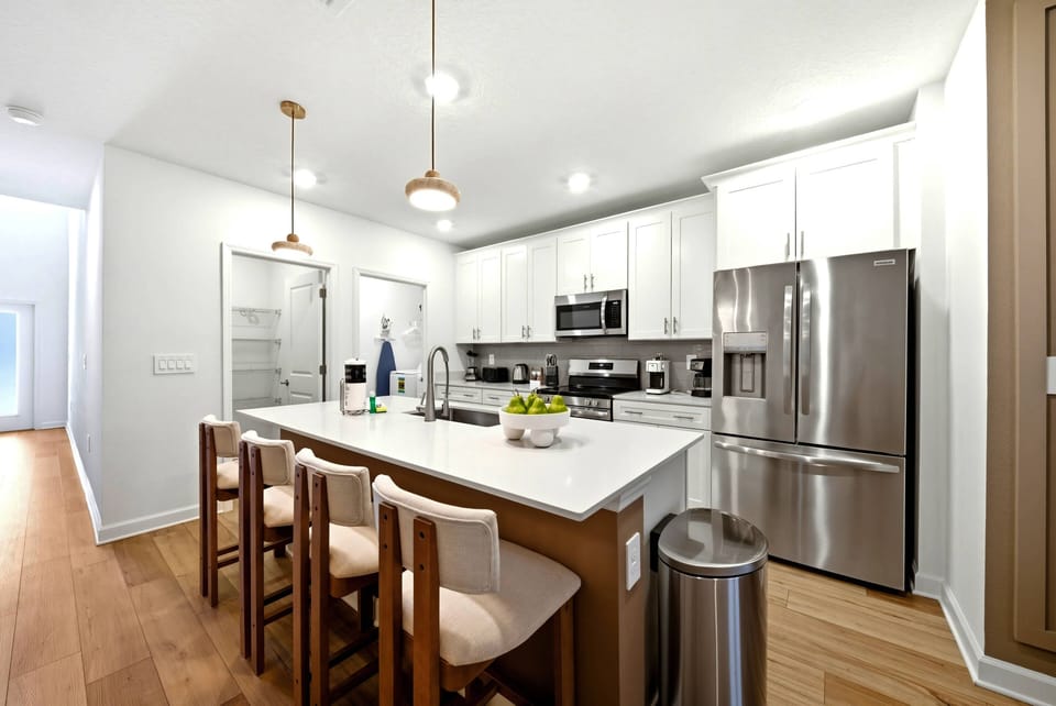 This inviting kitchen boasts sleek white cabinets and a spacious island with comfy seating, ideal for casual meals or coffee. The warm wooden floors create a cozy atmosphere, while modern stainless steel appliances enhance your.