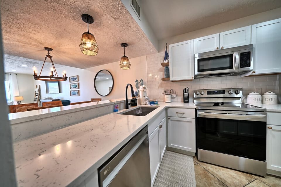 Sleek, fully equipped kitchen with stainless steel appliances and quartz countertops. Enjoy modern amenities like a dishwasher and microwave for easy meal prep. Accent lighting and an open layout connect to the inviting living area.
