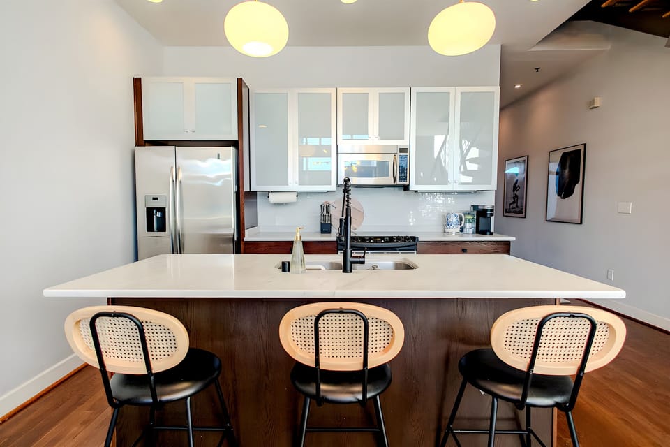 Pull up a stylish black and cane stool to the expansive kitchen island for a casual breakfast. The sleek white countertops provide plenty of room for meal prep or evening cocktails.