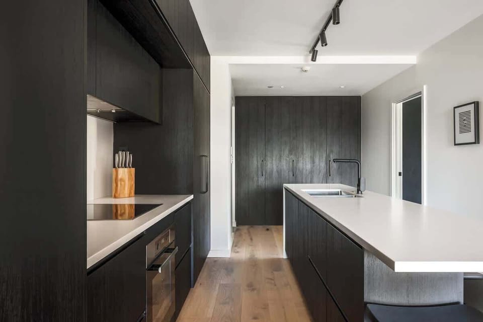 Gourmet kitchen at Clubhouse Lane, Jacks Point Golf Course. Sleek cabinetry, stone benches, premium appliances, open to living area with mountain lake views. Perfect Queenstown golf ski escape.