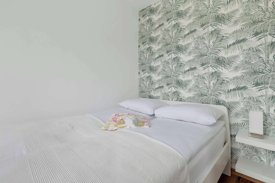 A bedroom with patterned wallpaper and a neatly made bed. Simple and comfortable space.
