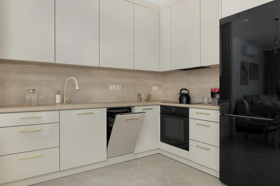 A close-up shot of a kitchen shows cream-colored cabinetry and dark countertops. The L-shaped corner features a black sink, oven, and refrigerator. A modern pendant light hangs over the dining area.