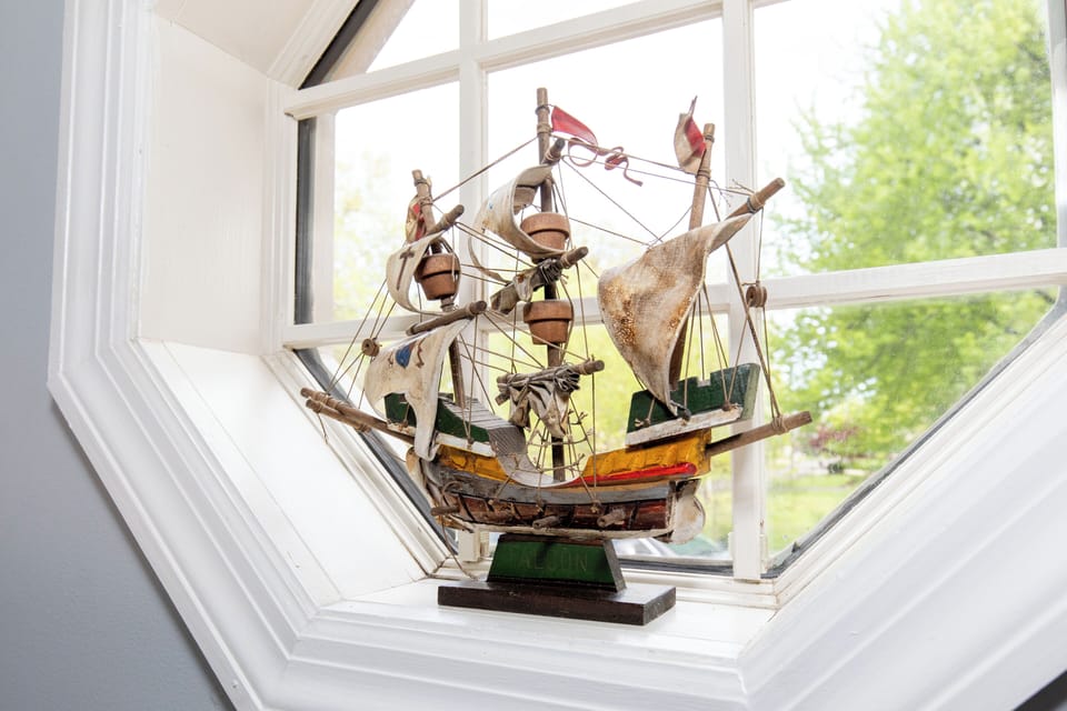 A charming vintage ship model rests on the windowsill, adding a touch of nautical character to your space while bright natural light floods in from outside.