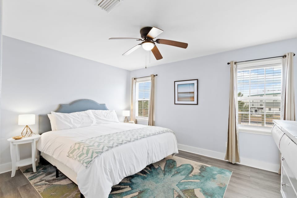 Sunny king bedroom with coastal decor, ceiling fan, and dresser