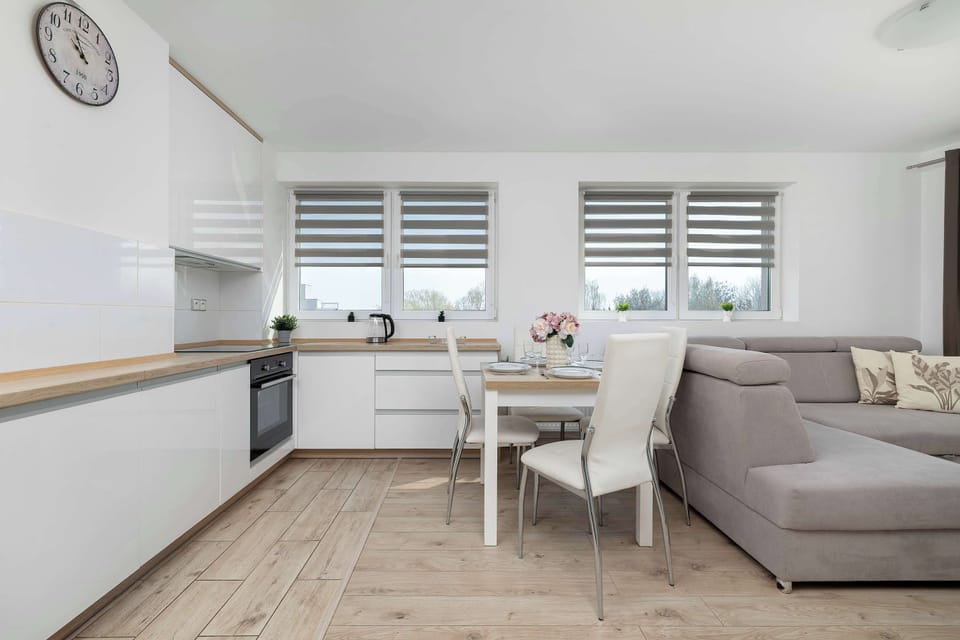A functional dining area consists of a white table and chairs positioned between the kitchenette and the lounge zone.