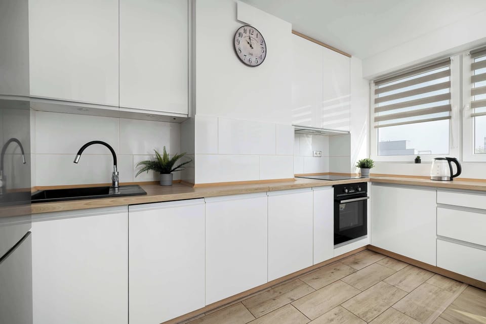 A modern white kitchenette showcases minimalist cabinetry, a light wooden countertop, and integrated appliances.