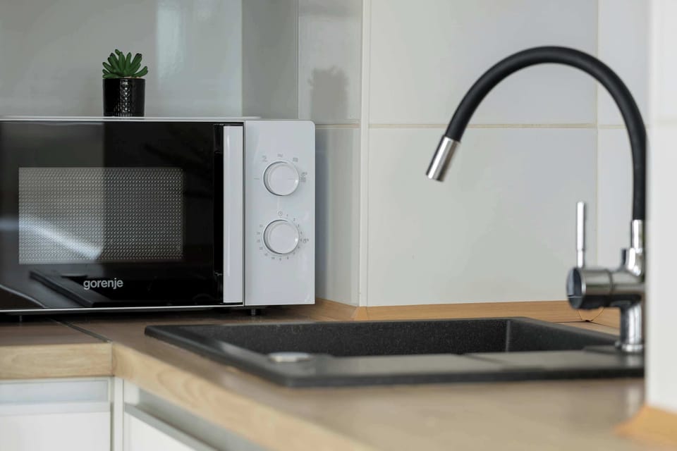 A close-up shot focuses on a modern black kitchen faucet and a microwave oven.