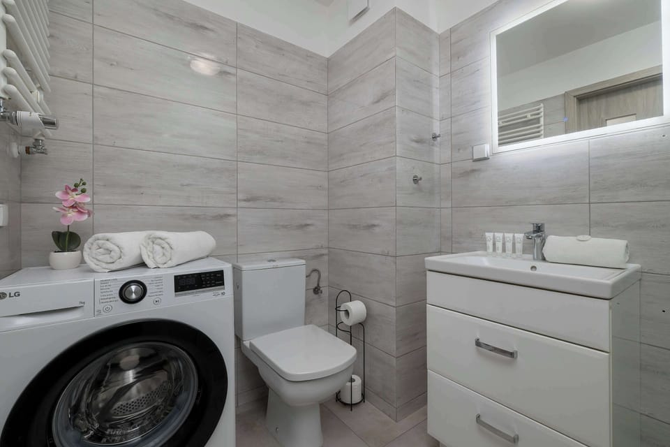 The bathroom includes a functional laundry area with a modern washing machine and light grey tiled walls