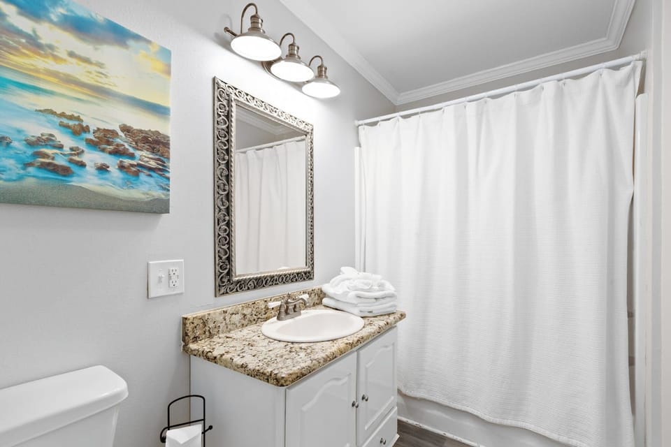 Sunny bath with granite vanity, fresh towels, and shower/tub combo.