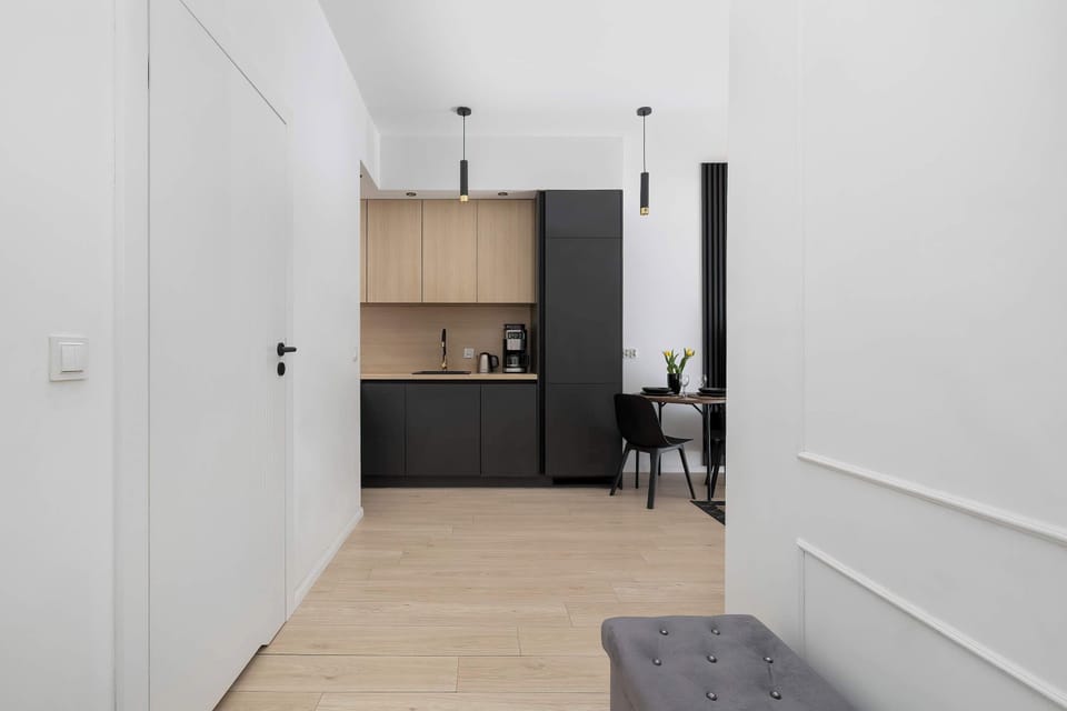 A hallway leading into a kitchenette with built-in cabinets and appliances. Light colors and simple finishes make the space feel open.