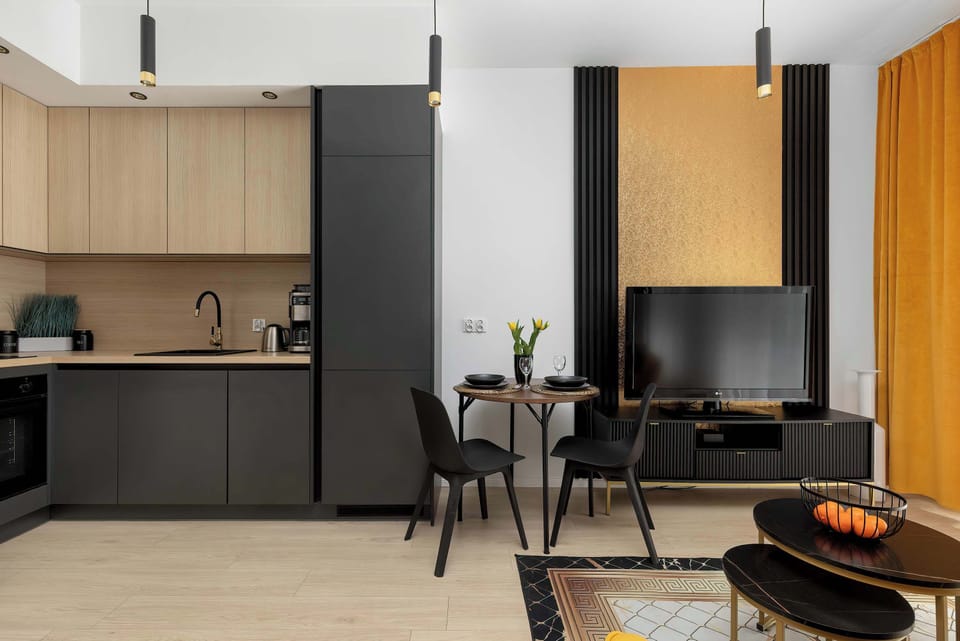 A living space combined with a kitchenette corner, featuring contemporary furniture and lighting. The layout is practical and well-organized.