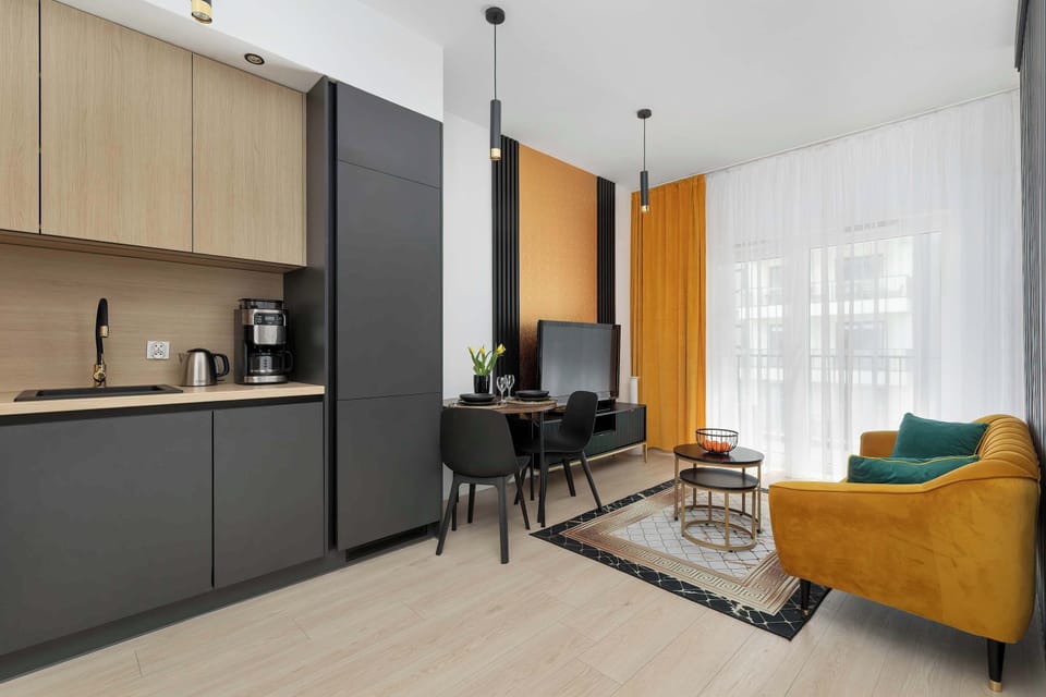 A modern living area connected to a kitchenette, with sleek cabinetry and neutral tones. A sofa and TV corner provide a comfortable place to relax.