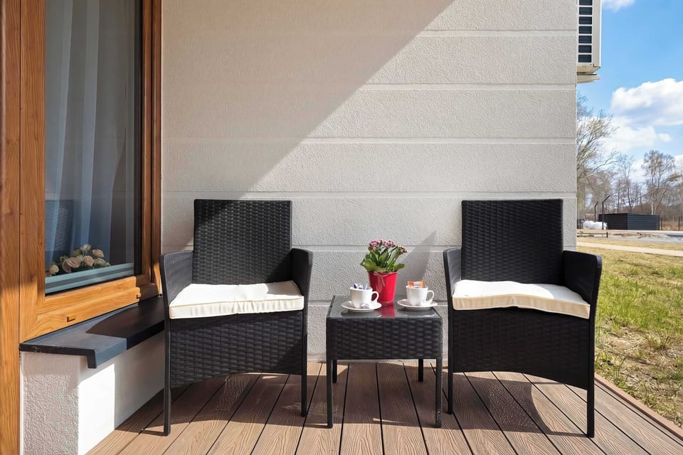 A centered view of the balcony highlights the black seating arrangement and the view of the surrounding landscape. The light-colored textured wall of the building complements the wooden decking.