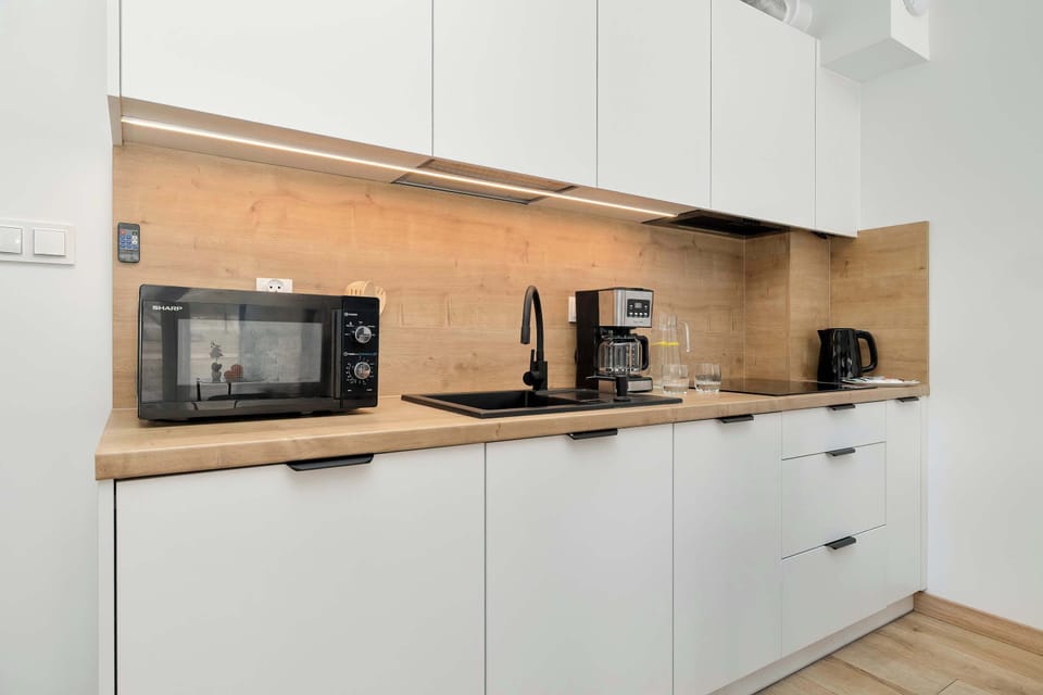 A close-up of the kitchenette highlights the wood-textured backsplash and modern appliances, including a microwave and coffee maker. Under-cabinet lighting illuminates the workspace effectively.