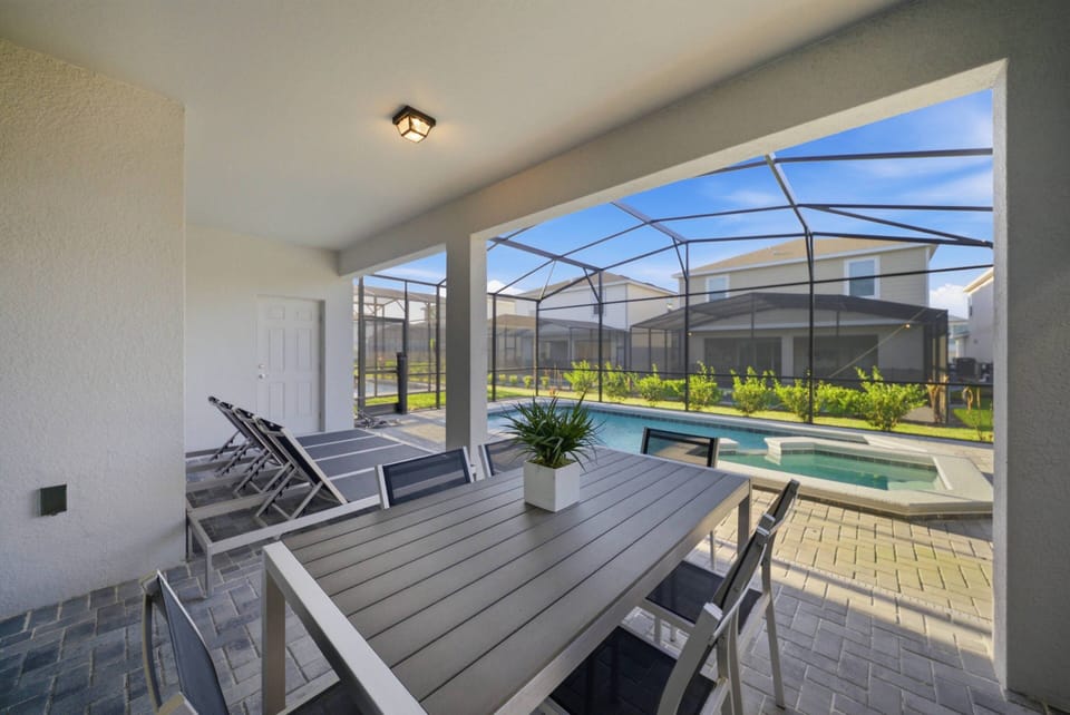 Savor your meals in our chic outdoor dining area, featuring modern furniture and a screened enclosure that offers comfort and stunning views of the inviting pool and lovely landscaping—perfect for relaxation.