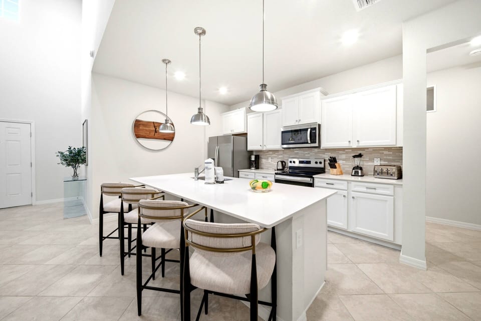 Discover a chic kitchen with sleek white cabinetry and a spacious island with modern bar stools, ideal for casual dining. The polished countertop and warm lighting create a welcoming ambiance perfect for gatherings.