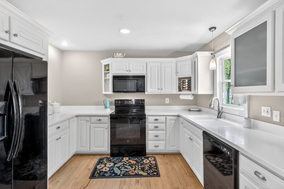 Cook with ease in this bright kitchen, featuring crisp white cabinets, sleek black appliances, and durable wood floors.
