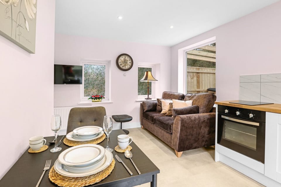 This cosy, open-plan living area features a modern kitchenette, a small dining table set for two, and a plush brown sofa.