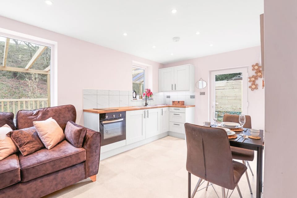 This compact open-plan living area combines a modern white kitchenette with a cosy dining nook and a brown leather sofa.