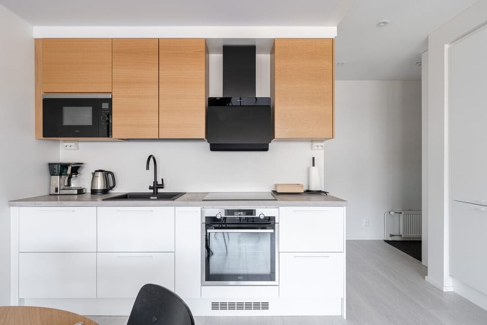 `Modern Scandinavian design at its finest. This fully equipped kitchen blends crisp white cabinetry with natural wood accents and premium black fixtures for a sophisticated, contemporary look