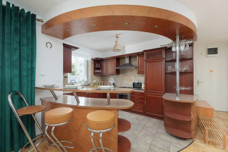 An open-plan kitchen  area with wooden cabinetry, curved countertops, and bar stools under warm lighting.