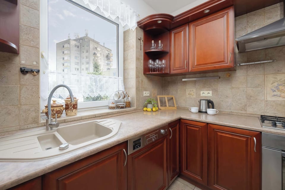 A compact kitchen corner with wooden cabinets, a sink by the window, and tiled walls.