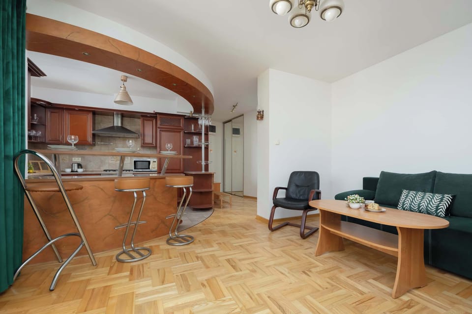 A spacious room combining a kitchen and living area with wooden floors and a curved bar dividing the space.