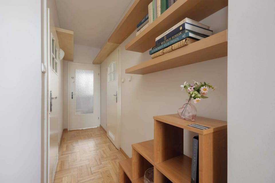 A hallway with wooden flooring, a small shelving unit, and simple decor elements.