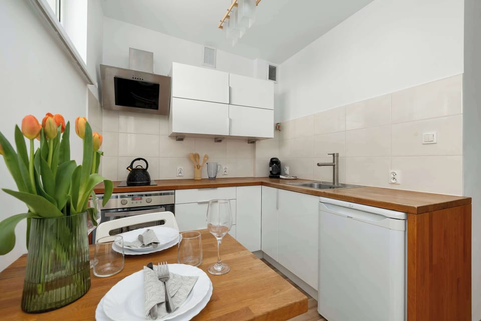 The compact kitchenette is designed with white upper cabinets and warm wooden countertops. A vibrant bouquet of orange tulips in a glass vase sits on the dining table, brightening the culinary space.