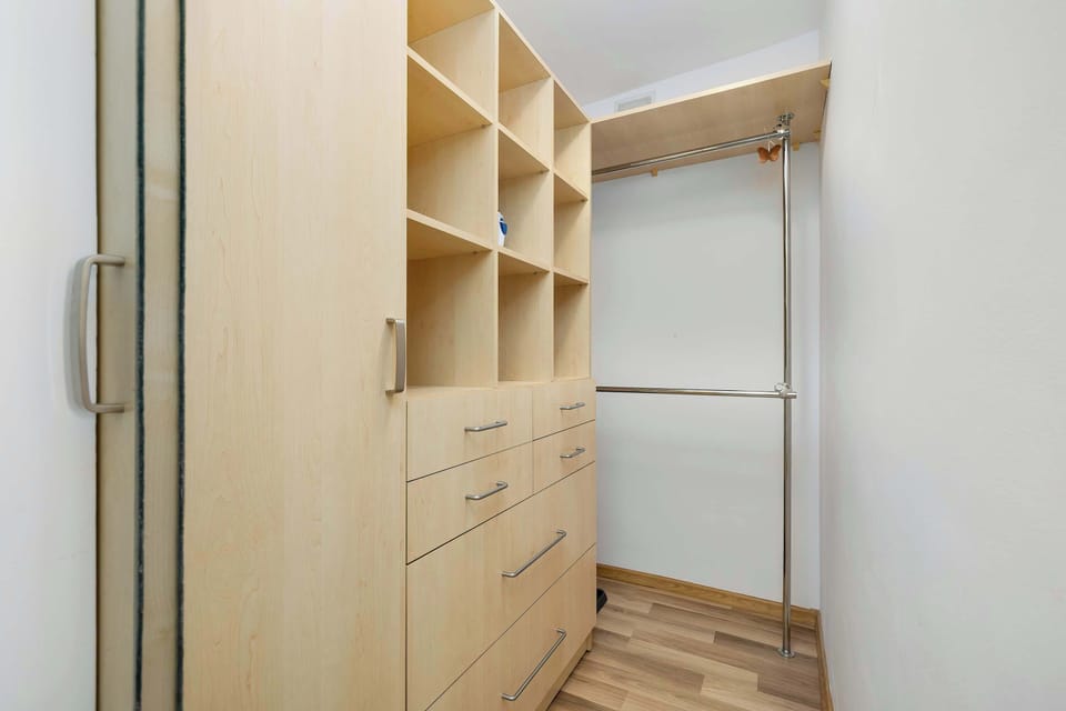 This walk-in closet or storage room is fitted with custom light-wood shelving and drawers. A hanging rail provides space for clothing, making the most of the vertical storage.
