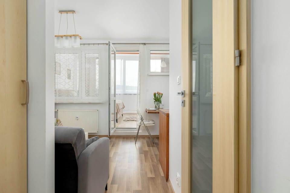 A doorway with a glass panel looks through to the living area, showing the transition between rooms. The light wood flooring continues throughout the apartment for a cohesive look.