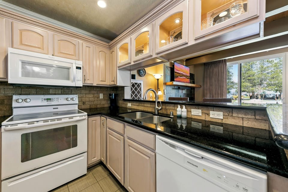 Your fully equipped kitchen features granite countertops, modern appliances, and warm lighting—perfect for preparing meals while enjoying views of the neighborhood through the large window.