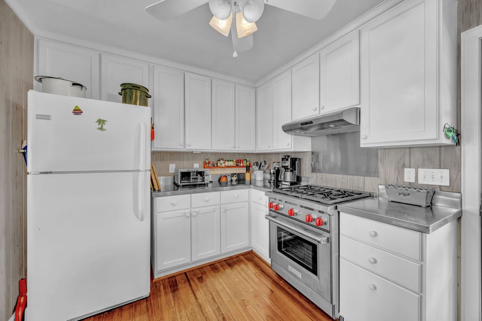 Your fully equipped kitchen features white cabinets, stainless steel appliances, and warm hardwood floors—perfect for preparing meals during your stay.