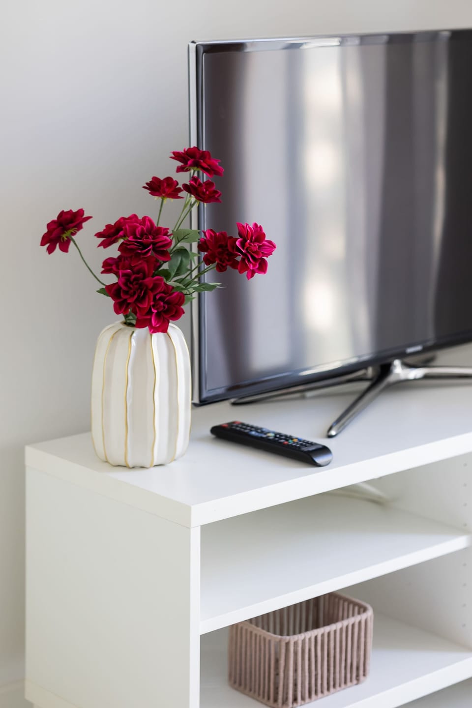 A close-up of a TV stand decorated with a vase of red flowers and minimalistic accessories.