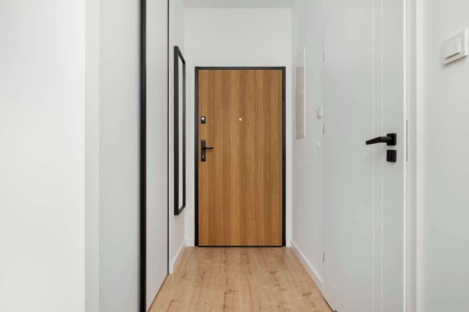 The entrance hallway features a light wood-finish door and white walls. The space is uncluttered and bright, providing a welcoming transition into the apartment.